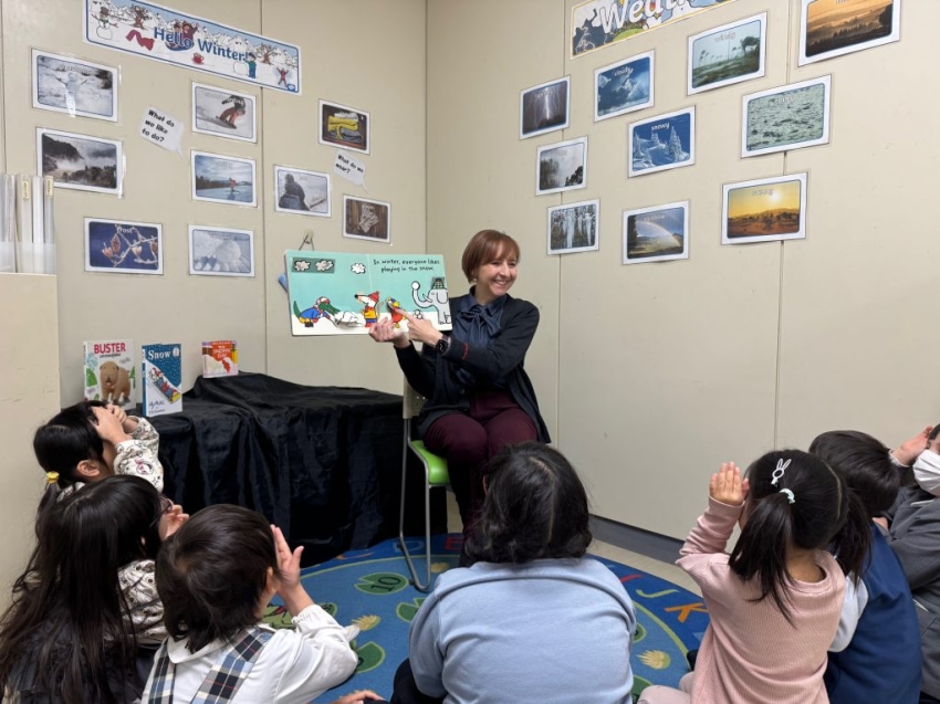 Teacher reading a picture book to a group of young children seated on the classroom floor.