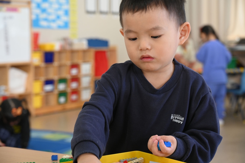 Young child concentrating while playing with small blocks at a classroom table.