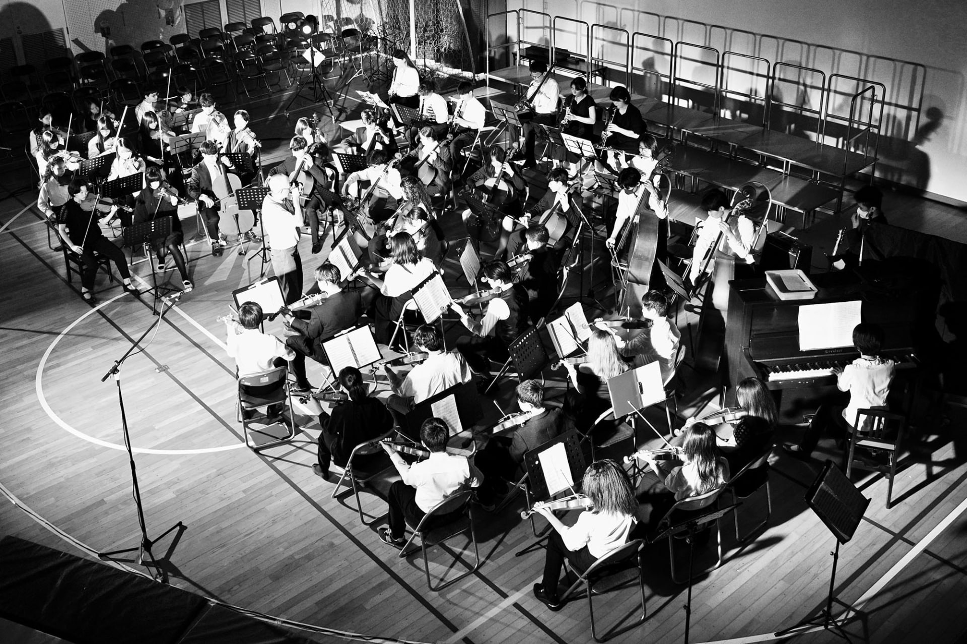 Large student orchestra performing on a stage in a school gymnasium.