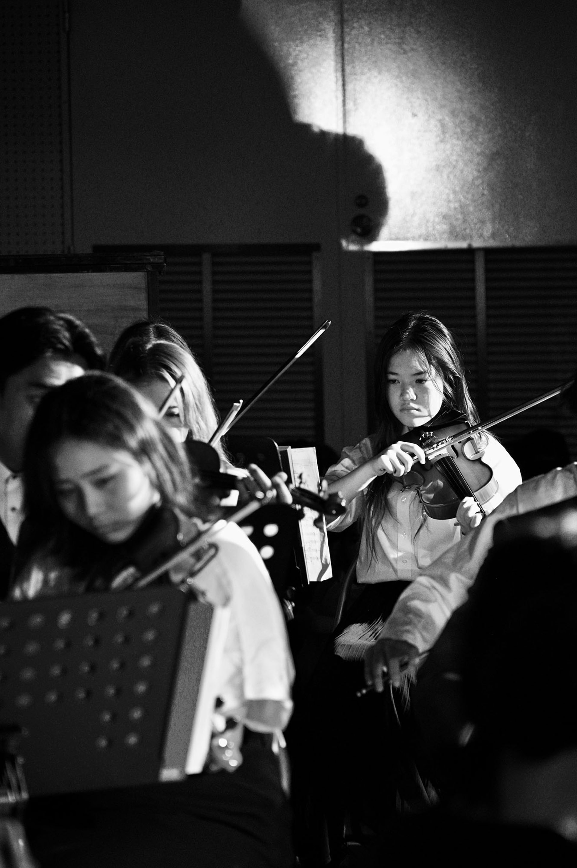 Students playing violins during a musical performance under stage lighting.
