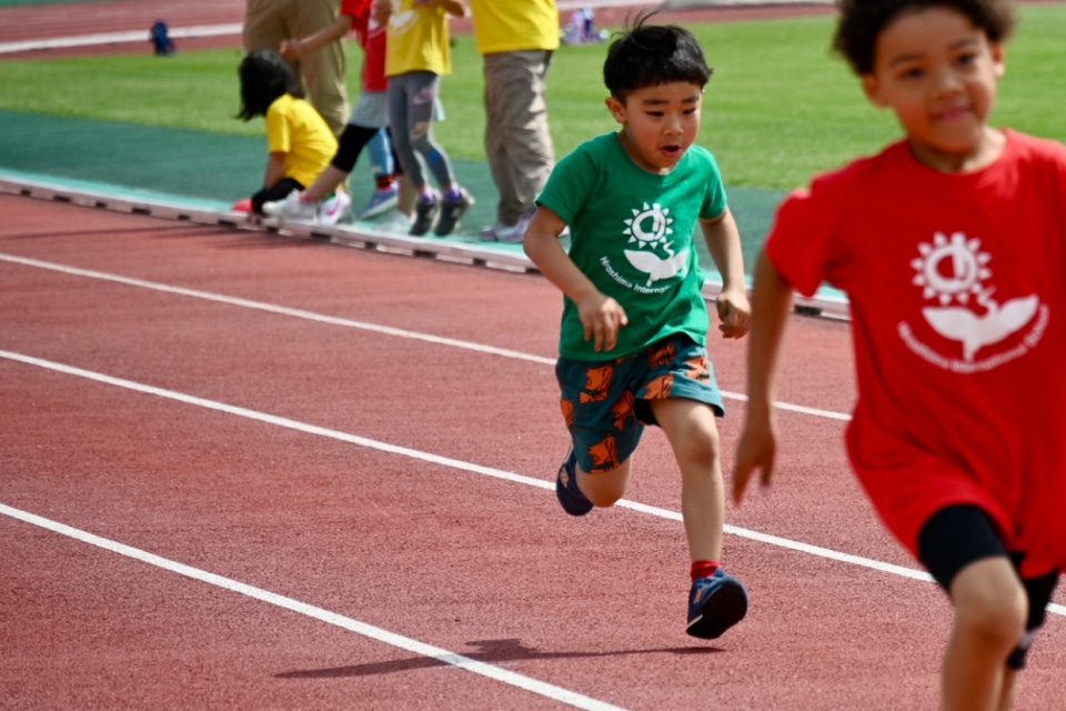Young children running on a track during a school sports day event.